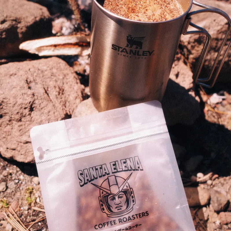 Bolsa de café Geisha de Santa Elena junto a un termo Stanley sobre las rocas