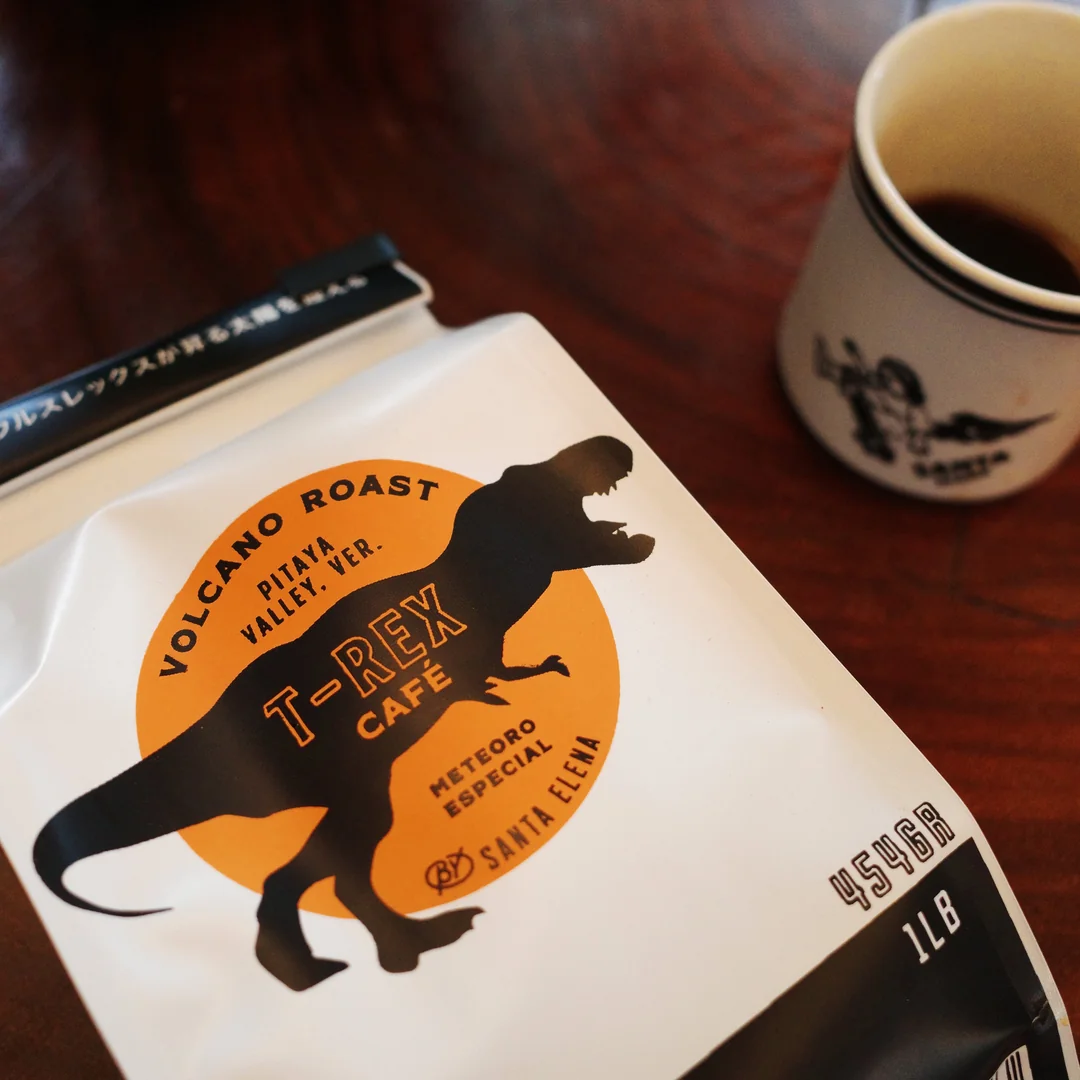Bolsa de café T-Rex Santa Elena junto a una taza sobre mesa de madera