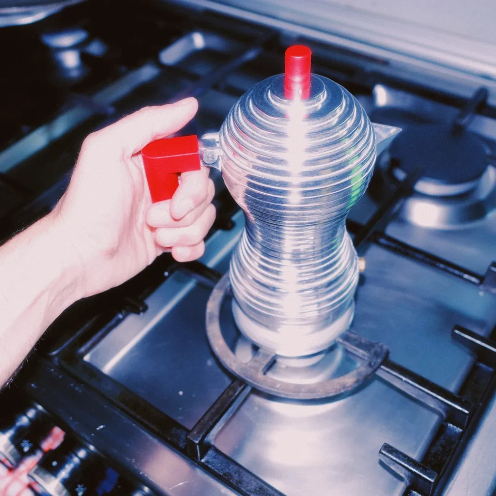 Cafetera Alessi Pulcina roja sobre la parrilla de una estufa de gas, sostenida por el asa