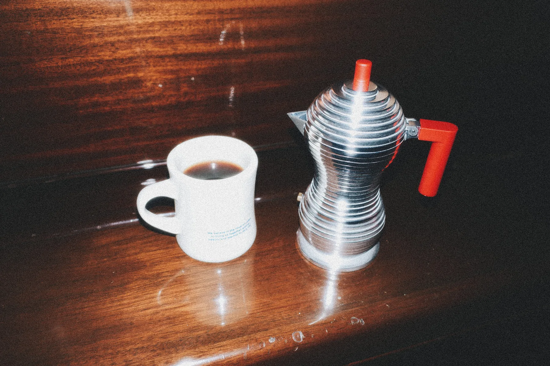 Cafetera Alessi Pulcina roja y una taza de espresso servido sobre una mesa de madera oscura