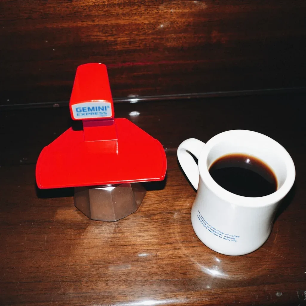 Cafetera Gemini Express roja junto a una taza blanca con café recién servido