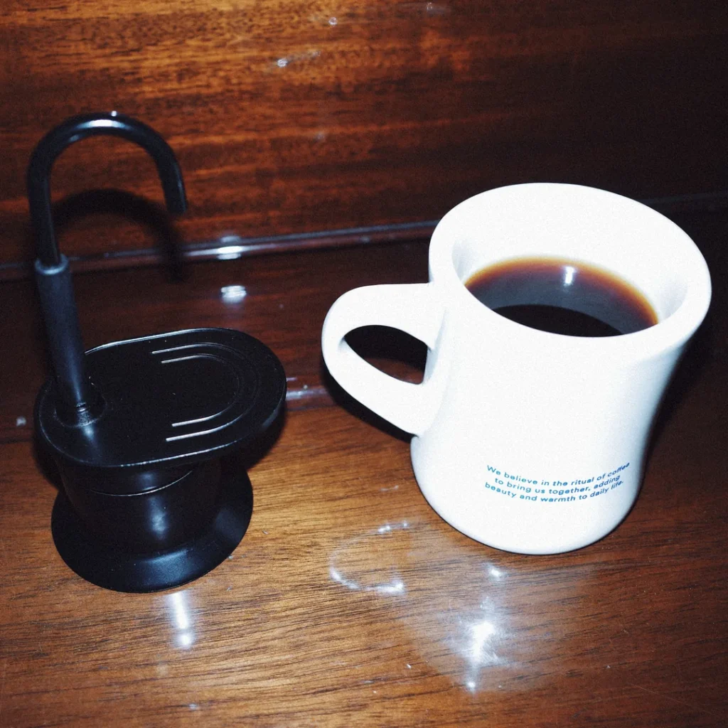 Cafetera moka negra junto a una taza blanca con café servido