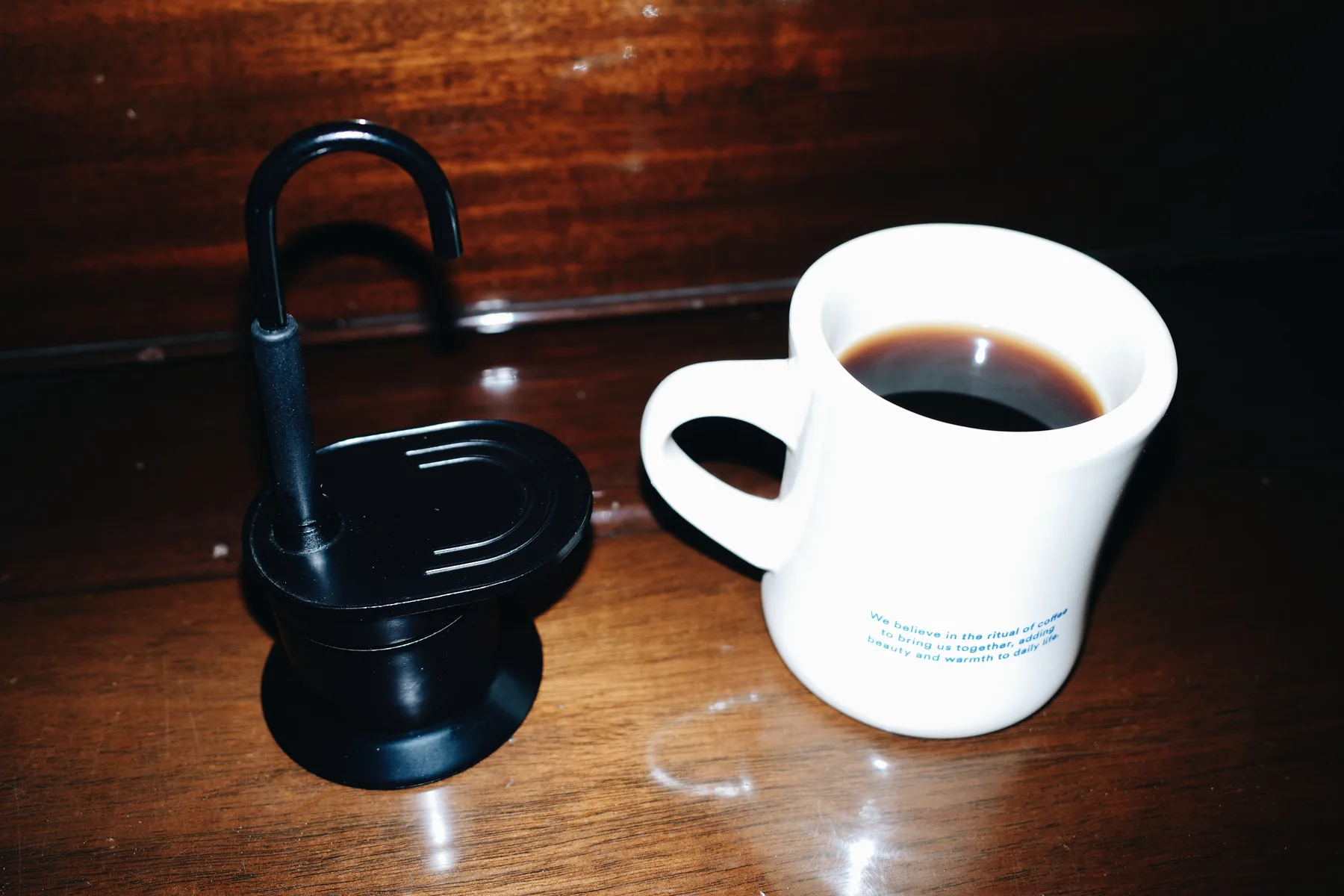 Cafetera moka negra y una taza de café sobre una mesa de madera