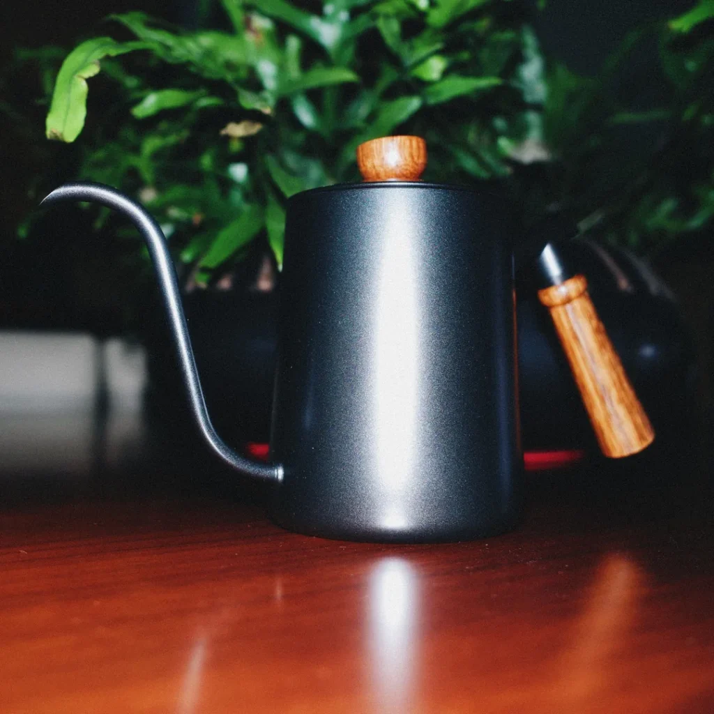 Jarra de cuello de cisne negra sobre una mesa, con una planta verde al fondo