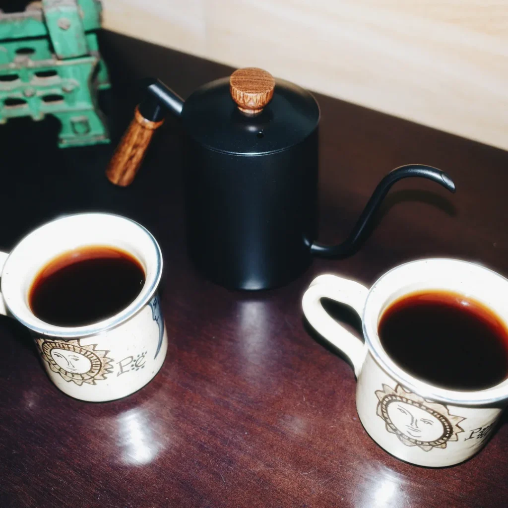 Jarra de cuello de cisne negra junto a dos tazas de café servido sobre una mesa de madera