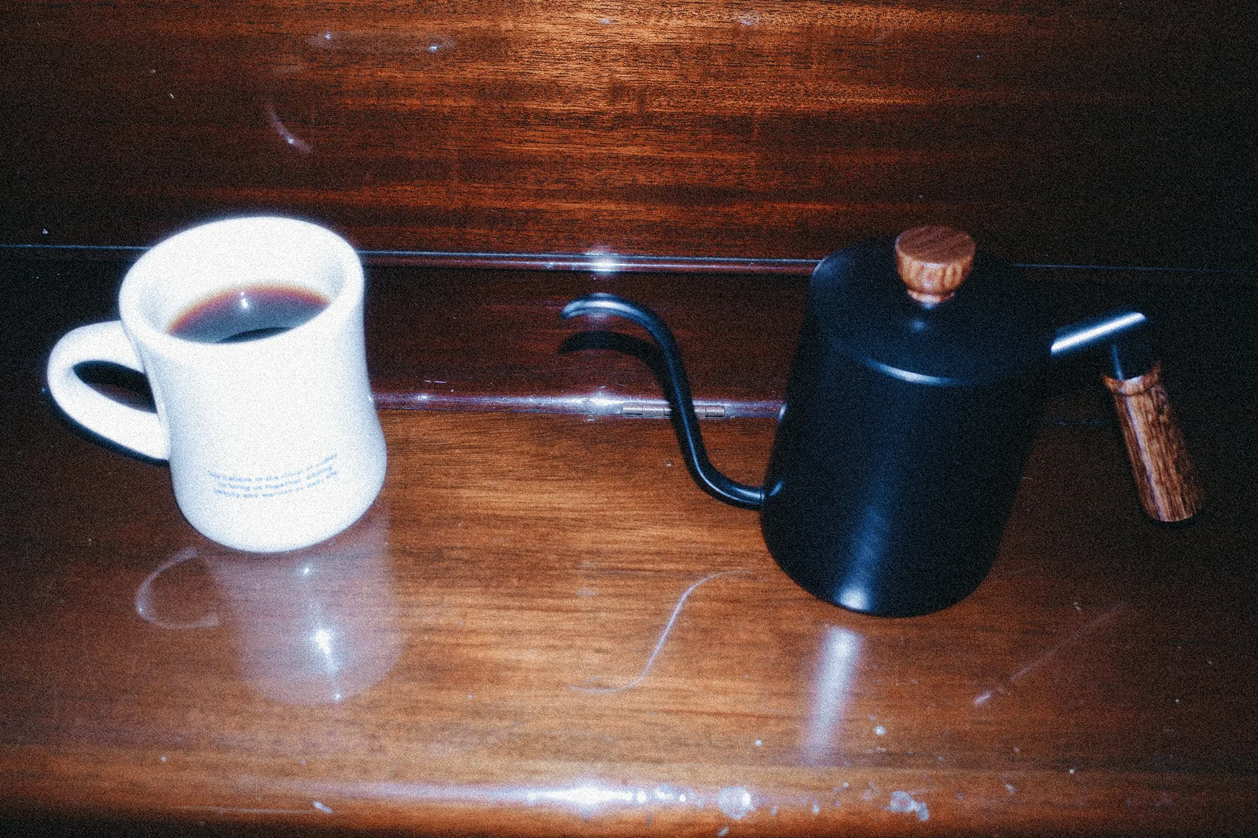 Jarra de cuello de cisne negra y una taza de café sobre una mesa de madera oscura