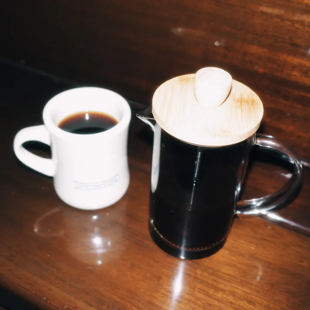 Prensa francesa con café preparado, junto a una taza blanca