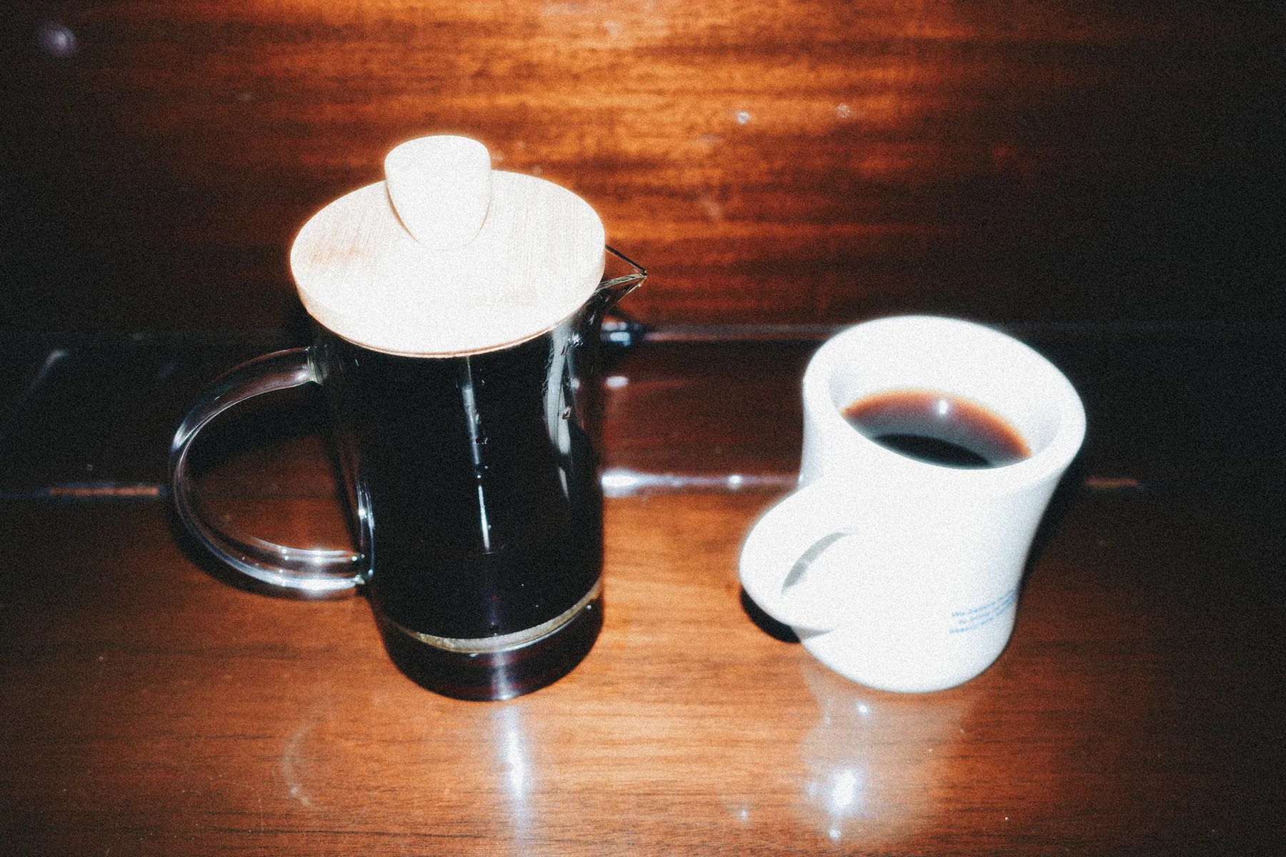 Prensa francesa y una taza de café sobre una mesa de madera